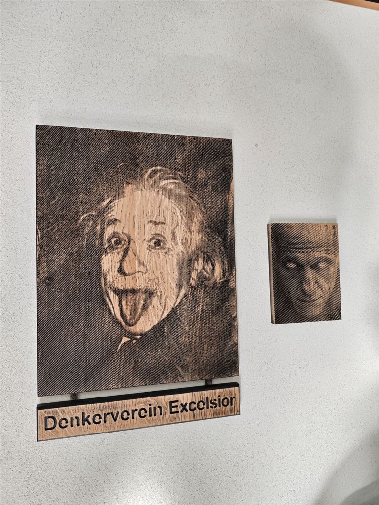 Einstein an der Wand – Wandbild mit Zusatzschild – feine Linienstruktur, die aus der Entfernung ein Portrait ergibt.